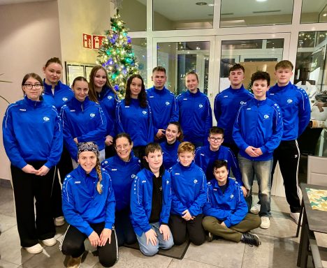 Gruppe von Jugendlichen in blauen Trainingsanzügen vor einem Weihnachtsbaum.