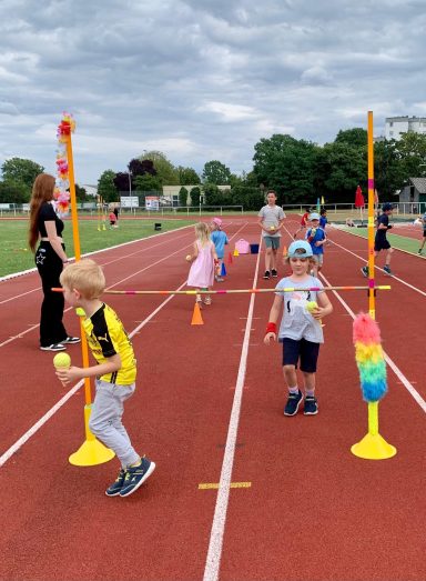 Kinder spielen auf einer Laufbahn, um Hindernisse mit bunten Stäben zu überwinden.