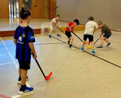 Kinder spielen Floorball in einer Sporthalle.