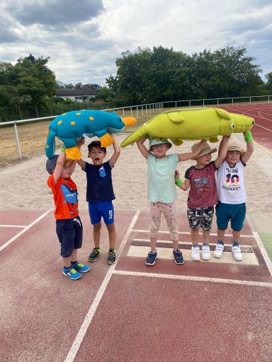 Fünf Kinder halten farbige Tierkissen über ihren Köpfen auf einer Laufbahn.