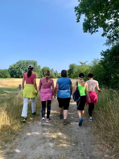 Fünf Personen in Sportkleidung gehen einen Feldweg entlang, umgeben von Natur.
