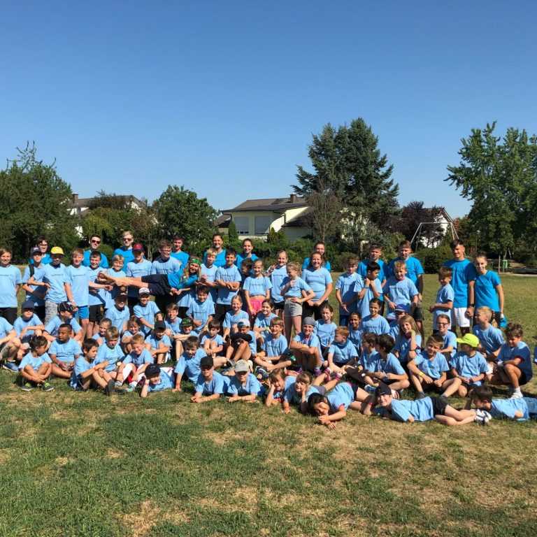 Gruppenfoto von Kindern und Betreuern in blauen T-Shirts auf einem grünen Feld.