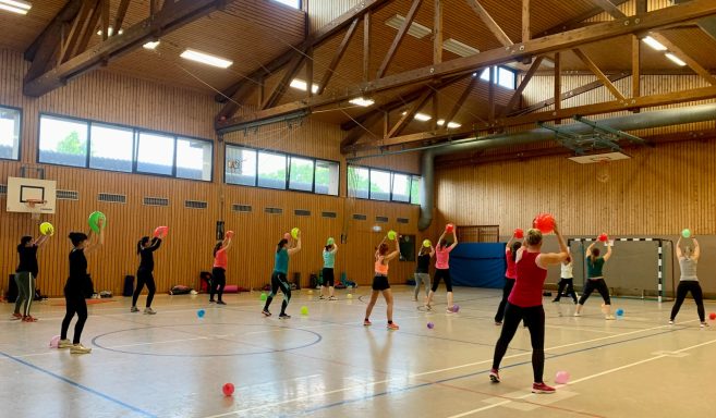 Gruppentraining in einer Halle mit bunten Bällen und motivierten Teilnehmern.